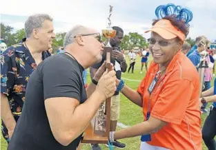  ?? JIM RASSOL/STAFF PHOTO ?? Patrick Moran, a member of the 1973 Hollywood Hills High School football team that won the state title that year, kisses the trophy, held by Dr. Maureen Lue as the team was honored Friday.