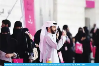  ?? — AFP ?? RIYADH: A Saudi man checks his mobile as women wait for their drivers outside a hotel in the Saudi capital on Sept 28, 2017.