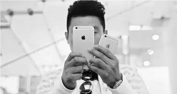  ?? PHOTO: REUTERS ?? REALITY BITE A man takes pictures as Apple iPhone 6s and 6s Plus go on sale at an Apple Store in Beijing last year. Apple’s rigidly self-contained iOS mobile operating system, which leaves little space for personalis­ation, has made it harder to attract...