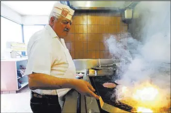  ?? SPENSER HEAPS/THE DESERET NEWS VIA AP ?? John Katzouraki­s works the broiler at Crown Burgers in Salt Lake City. He and his wife and their brothers, sisters, nephews and nieces own and operate seven restaurant­s.