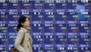  ?? — AFP ?? A pedestrian walks past an electronic stocks quotation board at an exchange in Tokyo.