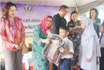  ??  ?? Juma’ani presents a school bag to one of the 435 pupils of SK Kampung Baru. On stage with her are (from left) Rosnie, Shan, Angelina and Leyta.