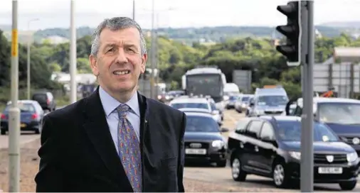  ??  ?? BOTTLENECK: David Stewart MSP at the Longman roundabout, Invermess, with a queue of A9 northbound traffic in the background