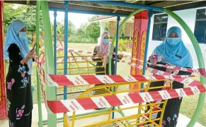  ??  ?? Access prohibited: Teachers at a Kemas kindergart­en in Mersing applying tape to a swing to prevent it from being used come July 1.