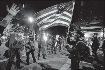  ?? SANCHEZ/ THE ASSOCIATED PRESS] ?? A demonstrat­or waves a U.S. flag Thursday in front of federal officers after tear gas is deployed during a Black Lives Matter protest at the Mark O. Hatfield United States Courthouse in Portland, Ore. [MARCIO JOSE