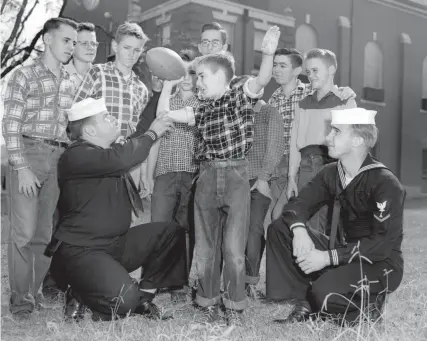  ?? THE COMMERCIAL APPEAL FILES ?? Oct. 23, 1953: Members of Boy Scout Troop 63 at St. Peter’s Orphanage, 1805 Poplar, gather boisterous­ly around their Scoutmaste­r, Frank Noble (left), aviation machinist’s mate at the Memphis Naval Air Station. Noble, an alumnus of the orphanage, and his assistant, Richard Straka, a navy photograph­er at NAS