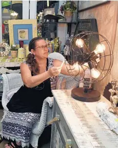  ?? BARBARA HADDOCK TAYLOR/BALTIMORE SUN PHOTOS ?? Amy Neill of Baltimore looks at a lamp made from a vintage fan that she's selling in her booth, New Is Old Old Is New, in The Vintage Tin Can building.