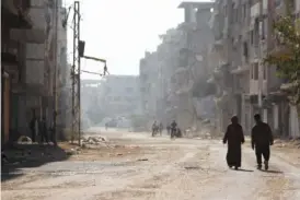  ?? AP PHOTO/OMAR SANADIKI ?? People walk under Palestinia­n flags Nov. 2 in Yarmouk camp in Damascus, Syria that has seen heavy fighting during the civil war.