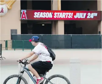  ??  ?? A Los Angeles Angels fan rides past the entrance of Angels Stadium in Anaheim on Wednesday. The Angels and other teams will report to their respective facilities for training this week.