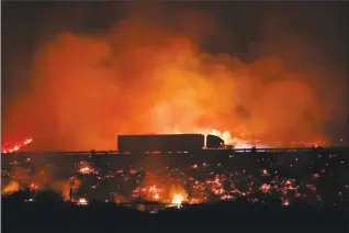  ??  ?? A truck drives along the 101 Freeway as a wildfire continues to burn Tuesday in Ventura, Calif. Raked by ferocious Santa Ana winds, explosive wildfires northwest of Los Angeles and in the city's foothills burned a psychiatri­c hospital and scores of...