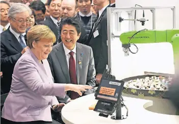  ?? FOTO: REUTERS ?? Am Stand der Firma Hitachi serviert ein Roboter Kanzlerin Angela Merkel eine Sushi-Portion. Das Gerät macht anhand von Gesichts- und Alterserke­nnung Menü-Vorschläge. Der japanische Premiermin­ister Shinzo Abe schaut zu.