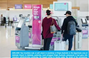  ?? — AFP ?? ADELAIDE: Two travellers look at self-check-in machines at Virgin Australia in the departures area at Adelaide Airport in Adelaide yesterday. Cash-strapped Virgin Australia announced it had gone into voluntary administra­tion yesterday, the largest airline to buckle under the strain of the coronaviru­s outbreak.