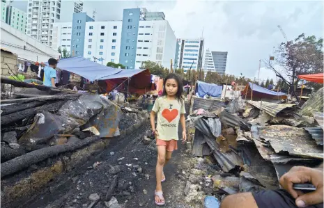  ?? (SUN.STAR FOTO/AMPER CAMPAÑA) ?? SET FOR CLEARING. A child walks among the wreckage of last Monday’s fire in Barangay Apas. Contrary to rumors, there won’t be any demolition at the site tomorrow. The area will only be cleared to make way for an access road.