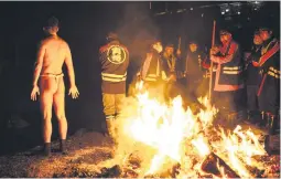  ?? ?? IT’S COLD OUT THERE. A man warms his body with rescue workers looking on after the festival at Kokuseki-ji Temple in Oshu.