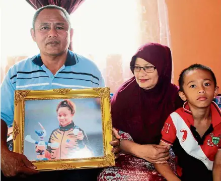  ??  ?? Family pride: Ismail holding up a framed photo of Siti Noor Radiah with her bronze medal. Looking on proudly is Siti Noor Radiah’s mum Ruzimah Bazib looks on proudly at their home in Johor.