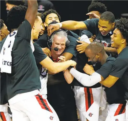  ?? K.C. ALFRED U-T ?? San Diego State players surround coach Brian Dutcher after beating Utah State to win the Mountain West Tournament on Saturday.