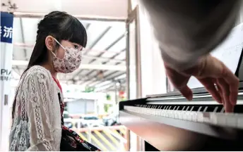  ??  ?? Yoyo wears a face mask during a piano lesson as Kam guides her through a piece of music in a ‘piano truck’.