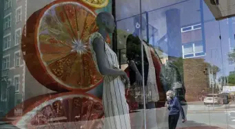  ?? AP ?? BOUNCE BACK: A passerby dons a mask as they walk past a storefront window on Tuesday in Cambridge. According to the Commerce Department, U.S. retail sales jumped by a record 17.7% from April to May.