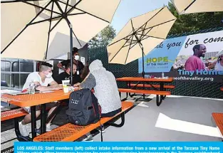  ?? —AFP ?? LOS ANGELES: Staff members (left) collect intake informatio­n from a new arrival at the Tarzana Tiny Home Village which offers temporary housing for people experienci­ng homelessne­ss in the Tarzana neighborho­od of Los Angeles.
