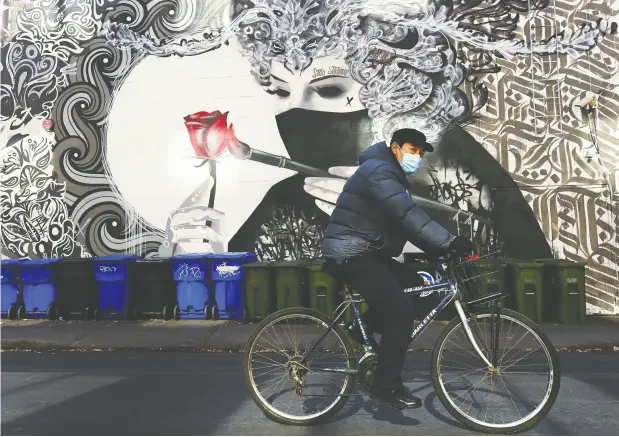  ?? Nathan Denett e / the canadian press ?? A man wearing a protective mask rides his bicycle past a masked mural in Toronto earlier this month.