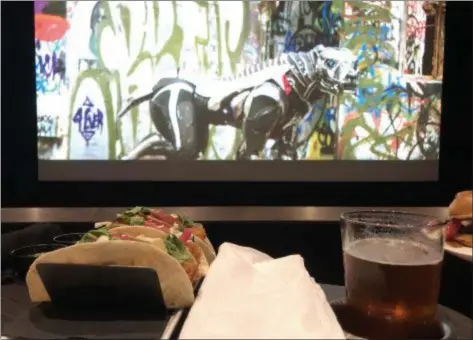  ?? MARK MESZOROS — THE NEWS-HERALD ?? A movie trailer plays as food and a beer sit on a tray at Silverspot Cinema.