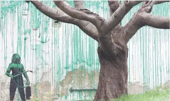  ?? Photos — AFP ?? A Banksy artwork is pictured, a stencil of a person having spray painted tree foliage onto a wall behind a leafless tree, a graffiti artwork confirmed as being the work of the famous street artist near Finsbury Park in north London.