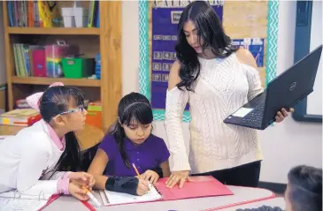  ?? ADOLPHE PIERRE-LOUIS/JOURNAL ?? Albuquerqu­e Bilingual Academy Teacher Ashley Torres works with 9-year-old students Yaritzel Hernandez, left, and Ashley Esqueda on Tuesday