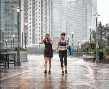  ?? TAMIR KALIFA / AMERICAN-STATESMAN ?? Adrianne Franscini (left) wipes rainwater away from her face as she and Elizabeth McKibbon cross the Pfluger Pedestrian Bridge during heavy showers Sunday morning.