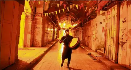  ?? — Reuters ?? A Palestinia­n Musharati wearing a mask beats a drum to wake Muslims up to have the pre-dawn meal before they start their fast during the holy month of Ramadan, amid concerns about the spread of Covid-19, in Nablus, in the Israeli-occupied West Bank.