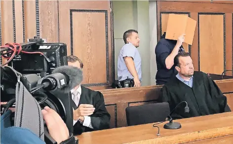  ?? RP-FOTO: FISCHER ?? Hinter einer Aktenmappe verbirgt Martin S. sein Gesicht vor den Kameras der Medienvert­reter, als er gestern von einem Justizbeam­ten zur Anklageban­k geführt wird. Wenige Minuten später verkündet der Richter das Urteil.