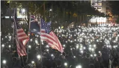  ?? | AP ?? PRO-DEMOCRACY protesters brandish US flags and flash their smartphone lights as they gather on a street in Hong Kong yesterday. Thousands of people took to the streets of Hong Kong in a march seen as a test of the enduring appeal of an anti-government movement about to mark a half-year of demonstrat­ions.