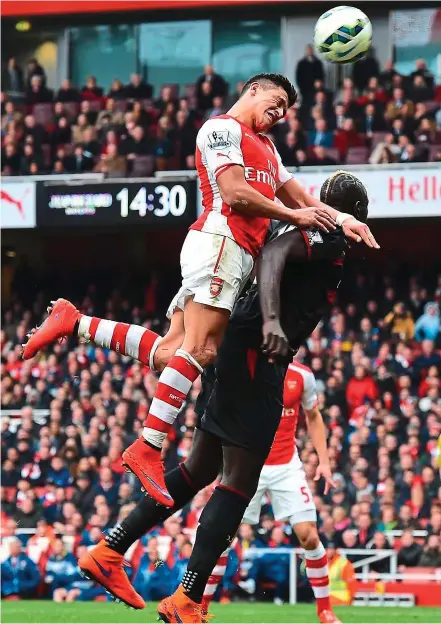  ?? — AFP ?? High point: Arsenal’s Alexis Sanchez wins a header against Liverpool’s Mamadou Sakho (right) during their English Premier League match at the Emirates on Saturday. Arsenal won 4-1.