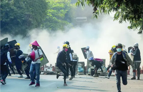  ?? AP ?? Los manifestan­tes se protegen de los gases lacrimógen­os lanzados por las fuerzas de seguridad ayer en Mandalay, Birmania