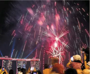  ?? — Reuters ?? Trying times: People watch as fireworks explode over Marina Bay during the National Day celebratio­ns in Singapore. The city-state is bracing itself for a protracted period of slacker growth and a drawn-out fight against inflation.