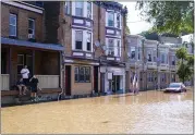  ?? MATT ROURKE — THE ASSOCIATED PRESS ?? People look at a flooded street as the Schuylkill River exceeds its bank in the East Falls section of Philadelph­ia, Sept. 2.