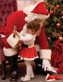  ?? CATHIE COWARD, THE HAMILTON SPECTATOR ?? Two-year-old Sofeara gets some help from Santa after her hat fell off at the police Christmas party Monday night at Carmen’s Banquet Centre.
