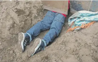  ?? JOHN MOORE/GETTY IMAGES ?? A migrant pulls himself under the U.S.-Mexico fence on Tuesday from Tijuana, Mexico.