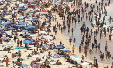  ?? GLENN CAMPBELL / AAP VIA REUTERS ?? Beachgoers sit on the sand and walk in the water at Sydney's Bondi Beach on a hot summer day on Sunday.