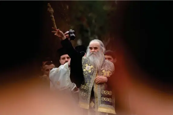  ?? (Reuters) ?? Metropolit­an bishop Amfilohije Radovic throws a wooden cross in the Ribnica river during Epiphany Day celebratio­ns