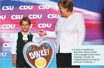  ?? AP ?? A boy in traditiona­l Bavarian attire hands over a gingerbrea­d heart reading ‘Thanks’ to Angela Merkel during an election meeting.