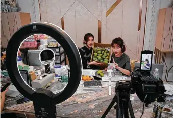  ?? Andy Wong / Associated Press ?? China's online celebrity Zhang Mofan, right, introduces fresh mangoes to her online clients and fans through livestream­ing from her house in Beijing.