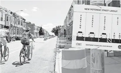  ?? AMY DAVIS/BALTIMORE SUN ?? Two cyclists ride past signage on South Potomac Street last summer explaining the designated use of the four lanes for parking, vehicular traffic and bicycles.