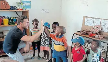  ??  ?? WELL DONE: A thrilled Cameron Bellamy high-fives a group of children at Sakhisizwe who took him through the head-to-foot naming of their body parts in isiXhosa and English.