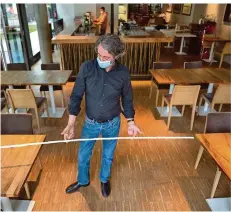  ?? FOTO: MARIJAN MURAT/DPA ?? Ein Wirt misst den Abstand zwischen zwei Tischen. Auch für Restaurant­s, die ab Montag wieder öffnen dürfen, gelten strenge Regeln.