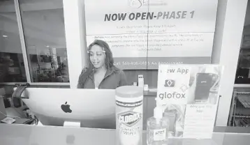  ?? JOHN MCCALL/SOUTH FLORIDA SUN SENTINEL ?? Fitness director Fabiana D'Antonio wears a mask at the front desk of Fitness Hub Studios as a way to protect customers and staff in West Palm Beach on Monday.