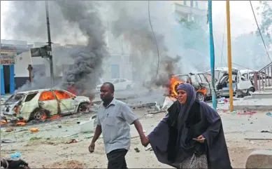  ?? FARAH ABDI WARSAMEH/ AP ?? A couple walk past burning vehicles after a suicide car bomb attack on a popular mall in Mogadishu, Somalia, on Sunday. A police officer said a car bomb blast near a police station in Somalia’s capital has killed at least five people and wounded at...