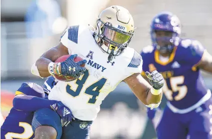  ?? JACOB KUPFERMAN/AP ?? Navy fullback Jamale Carothers tries to slip out of the grasp of an East Carolina defender Saturday during an AAC game in Greenville, N.C.