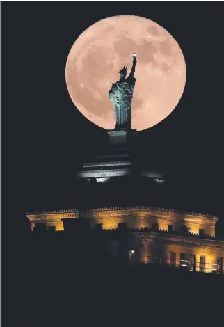  ?? Picture: AP ?? A supermoon rises in front of a replica of the Statue of Liberty sitting atop the Liberty Building in downtown Buffalo, New York.