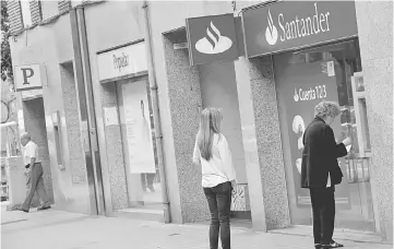  ??  ?? People use a Santander’s cash dispenser (ATM) as a man leaves a Banco Popular office in Barcelona, Spain Banco Santander is considerin­g compensati­ng some small shareholde­rs who lost all their investment in the buyout of Popular. — Reuters photo