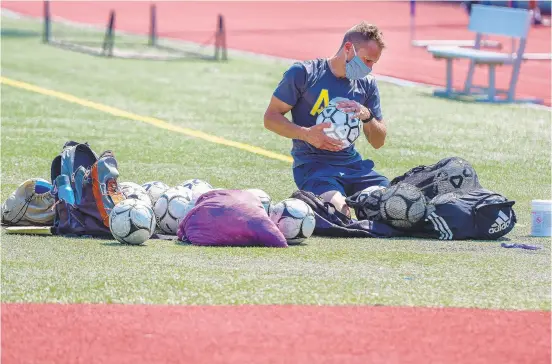  ?? RICK KINTZEL/THE MORNING CALL ?? Allen High School boys varsity soccer coach Jarrad Max wipes down the team’s soccer balls with disinfecti­ng wipes after practice Monday in Allentown.